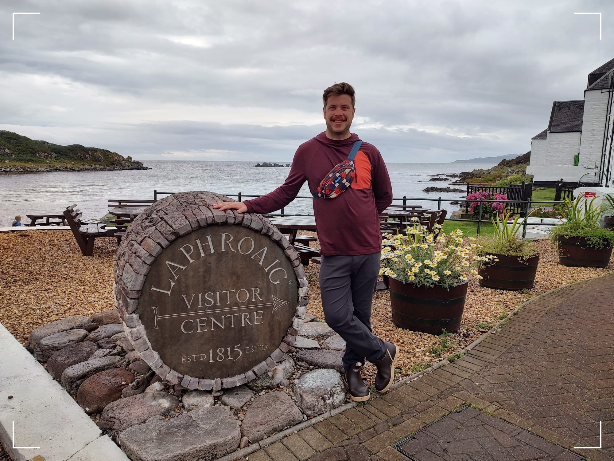 Me standing next to a barrel that says "Laphroaig Visitor Centre" with a background looking out to the sea.