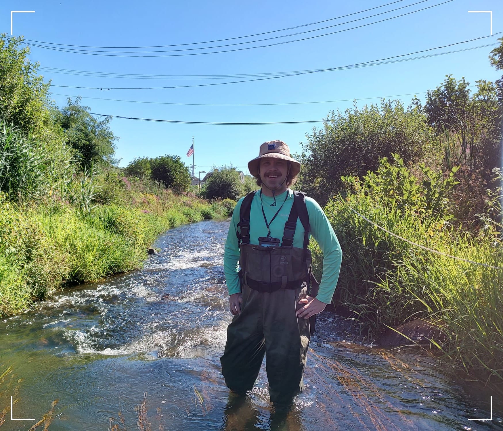 Me standing in knee deep water of a stream. The banks are covered in lush native vegetation.